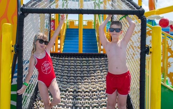 Two kids in colorful swimsuits playing joyfully on a sunny playground.