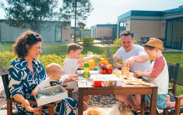 A happy family enjoying a picnic with food and drinks in a sunny outdoor setting.
