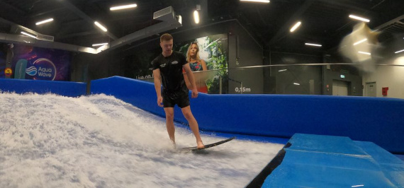 A man surfing on a wave in an indoor water park amidst splashing water.